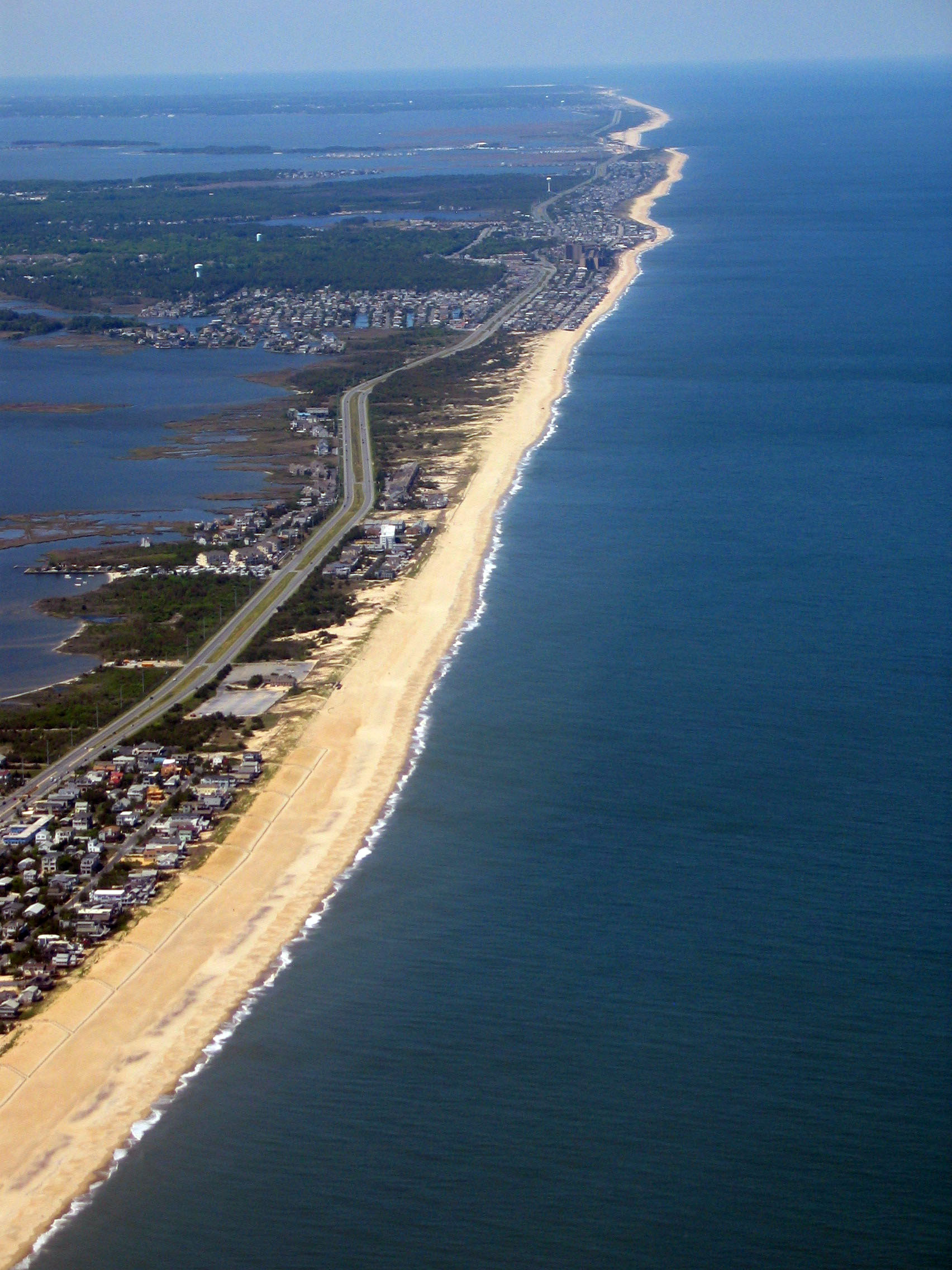 A town on a piece of land with the ocean on one side and a bay on the other. The land is very narrow and includes development and a sandbar.