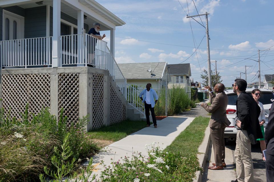 A man stands on his porch, talking to a group of people walking by in Edgemere, NY