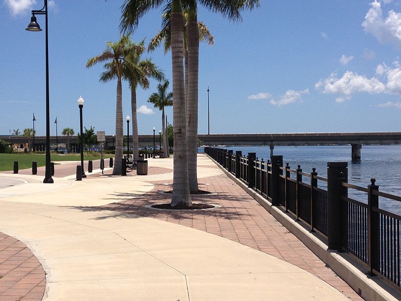 A harbor walk in Punta Gorda, Florida. The brick walkway is dotted with palm trees and streetlights, and the water is visible below.