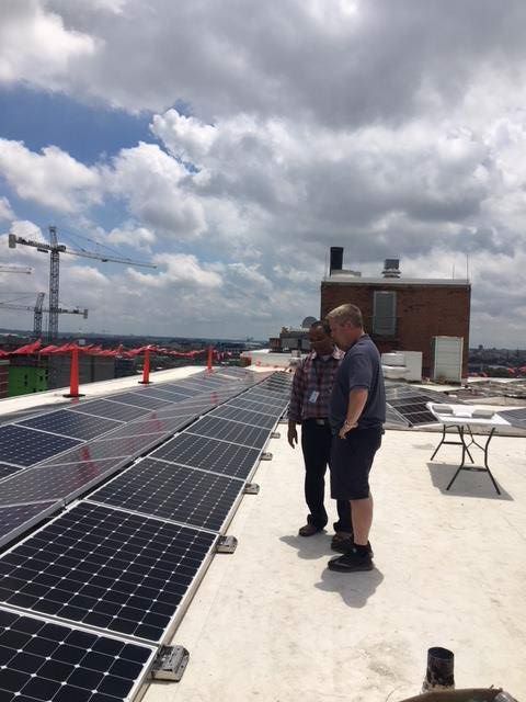 Two men stand on a rooftop by a recently installed solar energy array.