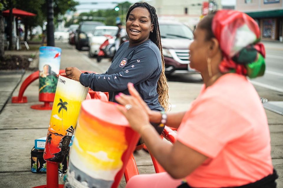 Two women joyfully play colorful drums as part of an art installation in Little Haiti, Miami.